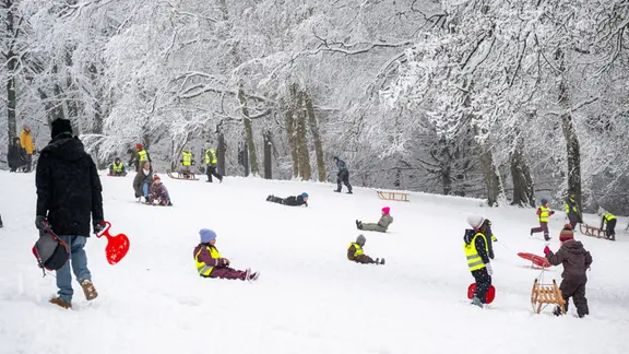 Viele Kinder rodeln einen Schneeabhang mit Schlitten runter. 