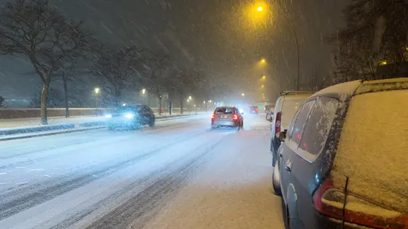 Schnee fällt in der Dunkelheit auf eine befahrene Straße am Hafen in Hamburg. | picture alliance/dpa | Bodo Marks Schnee fällt in der Dunkelheit auf eine befahrene Straße am Hafen in Hamburg.