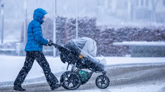 Eine Frau scheibt einen Kinderwagen durch Schneetreiben