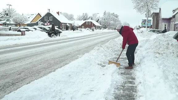 Eine Frau schippt Schnee an einer Straße.