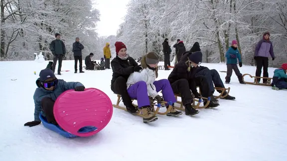 Erwachsene und Kinder rodeln im Schnee.