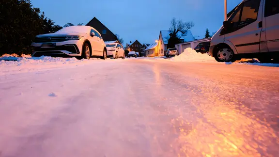 Mehrere Autos parken am Rand einer verschneiten Straße.