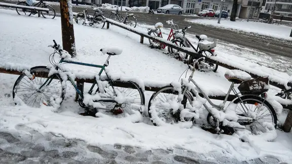 Schneebedeckte Fahrräder stehen an einer Straße.