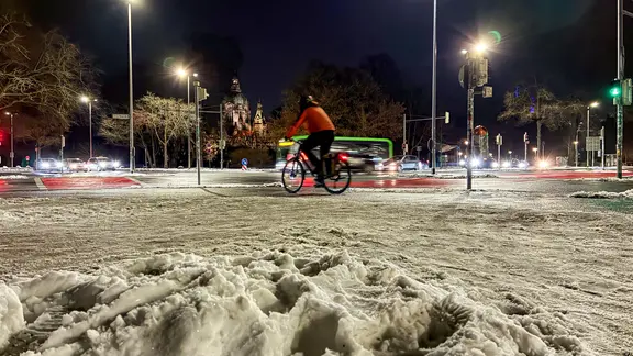 Eine Frau fährt am Abend mit einem Fahrrad durch das verschneite Hannover.