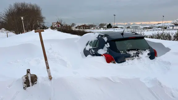 Eine abgebrochene Schaufel steht neben einem zugeschneiten Auto.