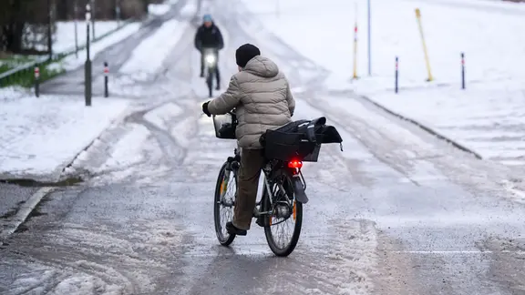 Eine Frau "schlittert" am Morgen mit ihrem Fahrrad über eine schneebedeckte glatte Straße.