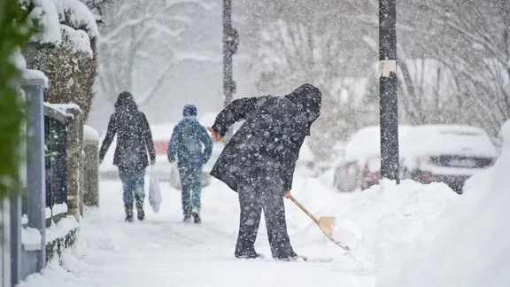 Bereits in den Morgenstunden müssen Hausbesitzer die Wege vorm Haus vom Schnee befreien. | picture alliance / dpa Themendienst, Tobias Hase Eine Frau befreit einen Gehweg vor ihrem Wohnhaus vom Schnee.