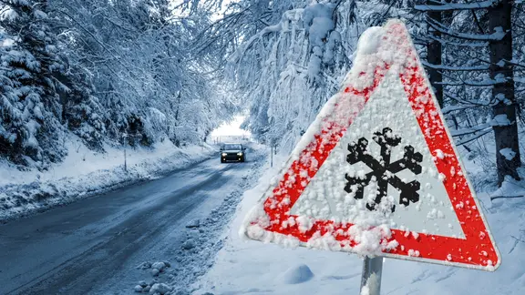 Ein eingeschneites Schild warnt an einer Straße vor Schnee und Glatteis. (Themenbild)