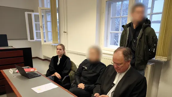 Eine Polizistin sitzt kurz vor Beginn eines Prozesses mit Anwälten in einem Gerichtssaal.