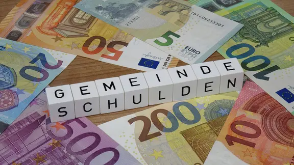 Geldscheine und Steine mit Aufschrift "Gemeinde Schulden"