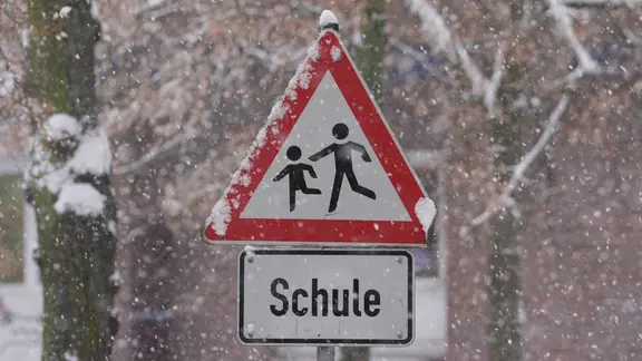 Ein Verkehrsschild "Achtung, Schule!" bei Schneefall.
