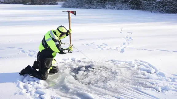 Ein Feuerwehrmann hackt ein Loch in einen zugefrohrenen See.