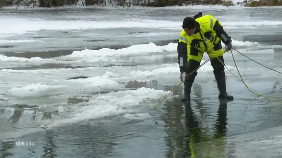 Ein Mann von der Polizei mit einem Seil auf einem vereisten Teich.