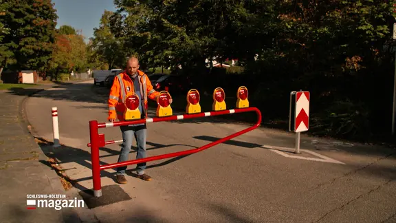 Ein Mann macht eine Schranke an einer Schulstraße in Kiel-Mettenhof auf.