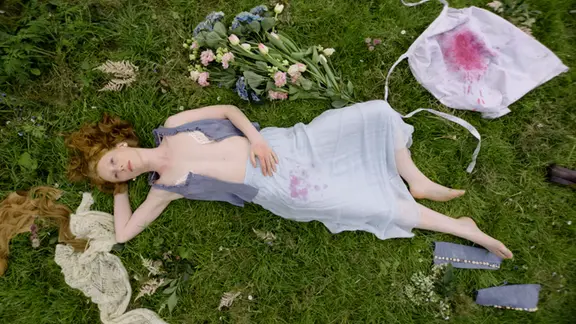 Szene aus dem Film "Smalltown Girl": Eine junge Frau liegt auf dem Rasen, ihr Kleid ist aufgerissen und mit Blut befleckt. Neben ihr liegen Blumen und ein blutiges weißes Tuch. | Neue Visionen Szene aus dem Film "Smalltown Girl": Eine junge Frau liegt auf dem Rasen, ihr Kleid ist aufgerissen und mit Blut befleckt. Neben ihr liegen Blumen und ein blutiges weißes Tuch.
