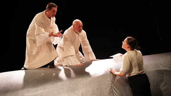 Zwei Männer in weißen gewändern sitzen auf dem Wal und reden mit einer Frau, die davor steht