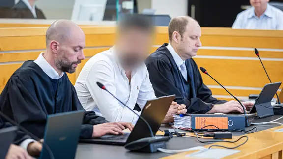 Angeklagter in einem weißen Hemd zwischen zwei Anwälten in einem Saal im Landgericht Hannover | picture alliance/dpa | Moritz Frankenberg, Moritz Frankenberg Angeklagter in einem weißen Hemd zwischen zwei Anwälten in einem Saal im Landgericht Hannover