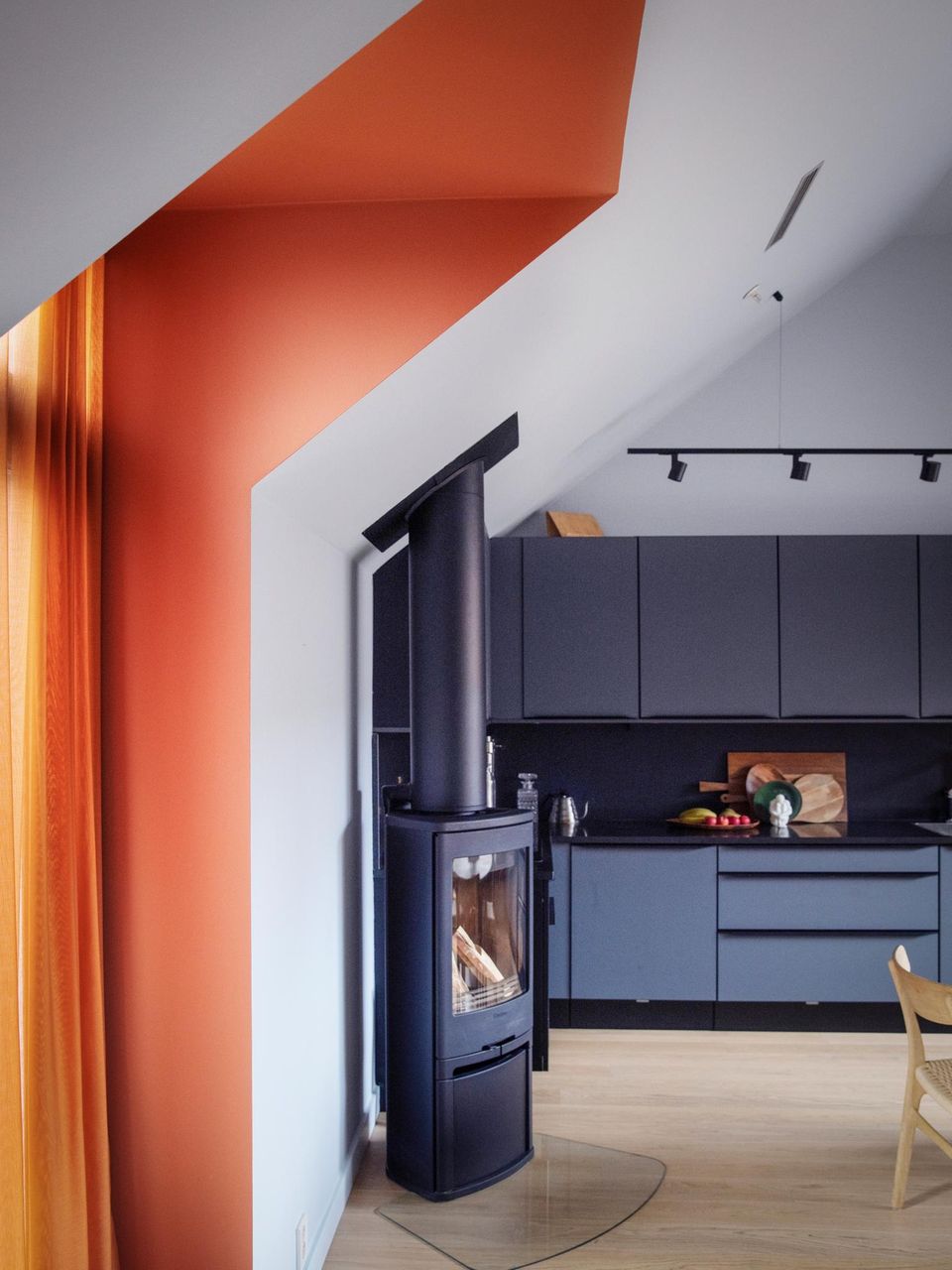 Raum mit blauer Küche, Holzofen und Dachschräge mit orangener Wand