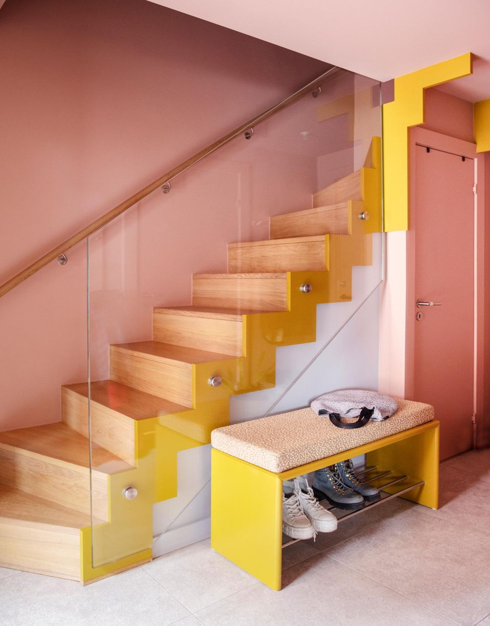 Treppenhaus mit rosa Wänden, Holztreppe mit gelben Akzenten und gelber Schuhbank