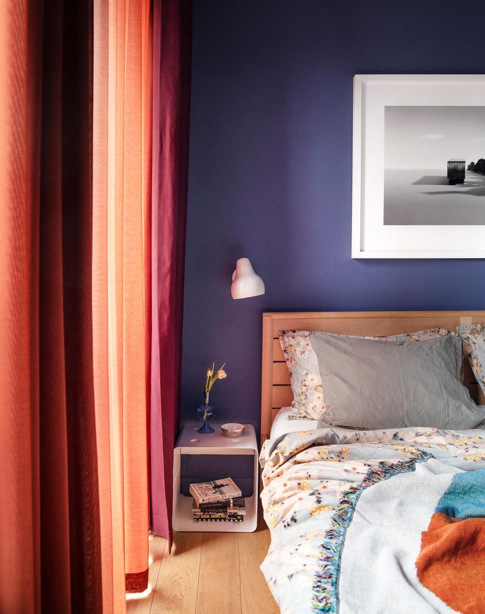 Bett vor einr dunkelblauen wand neben orangenen Vorhängen