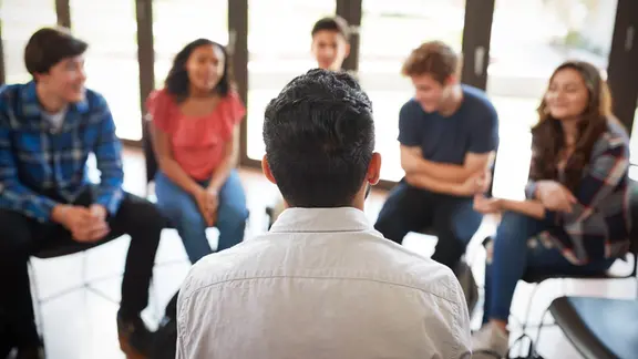 Ein Stuhlkreis mit einer Person im Zentrum des Bildes.