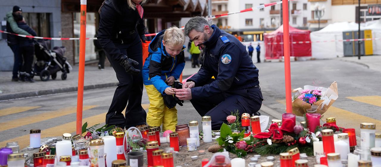Ein Polizist hilft einem Jungen beim Anzünden einer Kerze in der Nähe der Bar "Le Constellation" in Crans-Montana, Schweiz.
