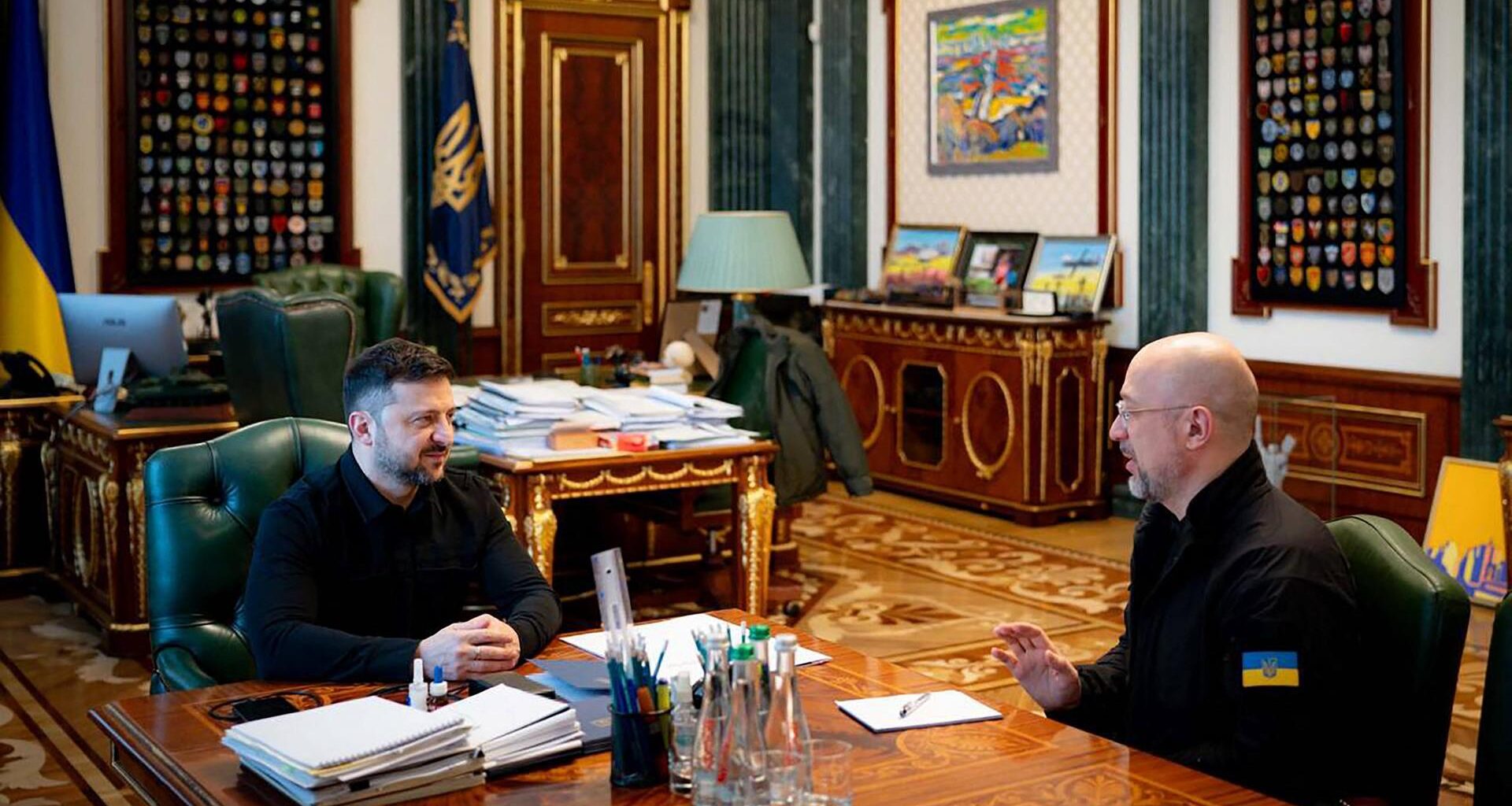 Selenskyj und Shmyal sitzen in einem Büro gemeinsam zu einer Besprechung am Schreibtisch.