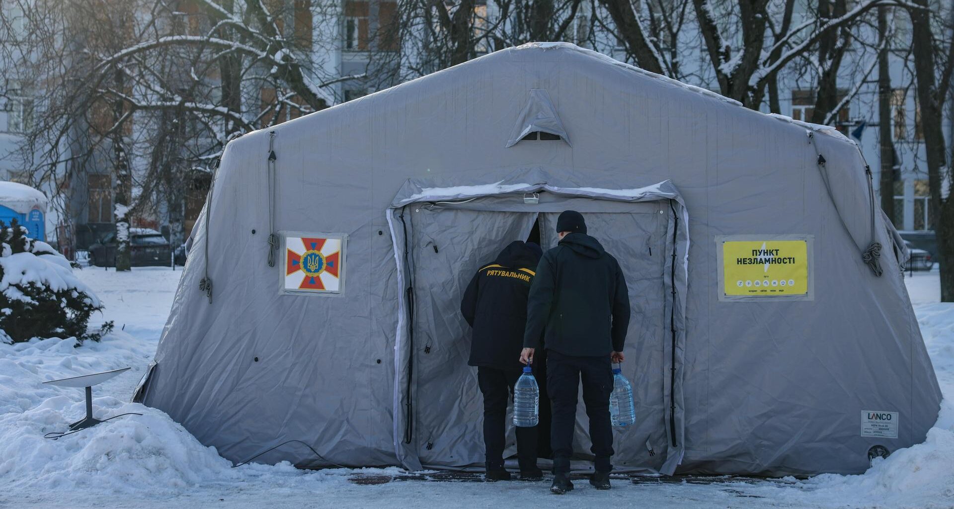 Zwei Männer gehen in ein großes, weißes Heizzelt, das von Schnee und Wohnhäusern umgeben ist.
