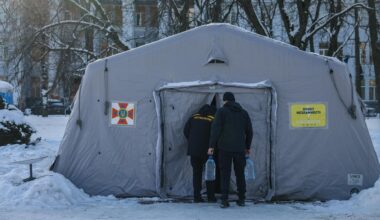 Zwei Männer gehen in ein großes, weißes Heizzelt, das von Schnee und Wohnhäusern umgeben ist.
