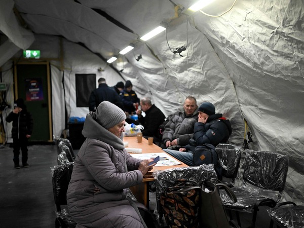 Local residents sit in a heated tent providing overnight accommodation for local residents whose apartments remain without heating due to recent Russian strikes damaging energy infrastructure in Kyiv on January 25, 2026, amid the Russian invasion of Ukraine. (Photo by Sergei GAPON / AFP)