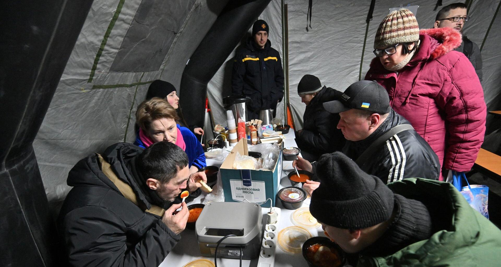 Menschen sitzen in Kiew in einem Zelt und nehmen eine warme Mahlzeit zu sich.