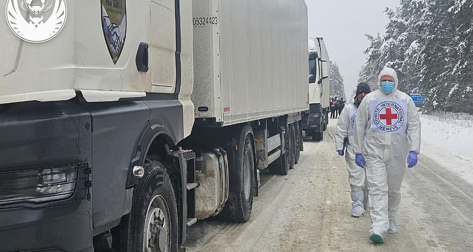 Mitarbeiter des UNHCR laufen neben weißen Lkw's.