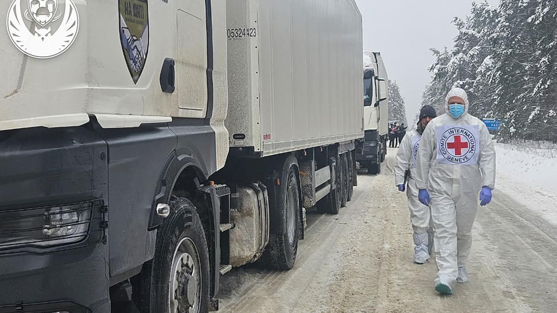 Mitarbeiter des UNHCR laufen neben weißen Lkw's.