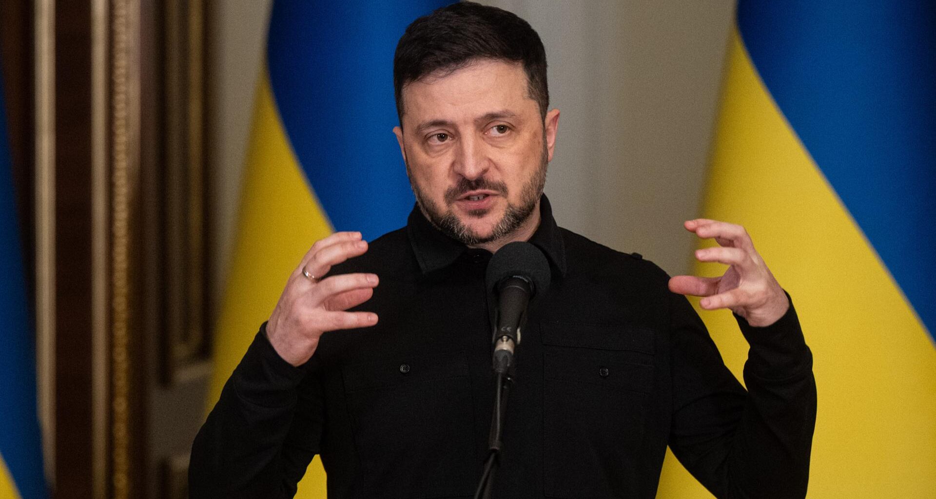 Wolodymyr Selenskyj, Präsident der Ukraine, spricht während eines Briefings. Hinter ihm sind ukrainische Flaggen zu sehen.