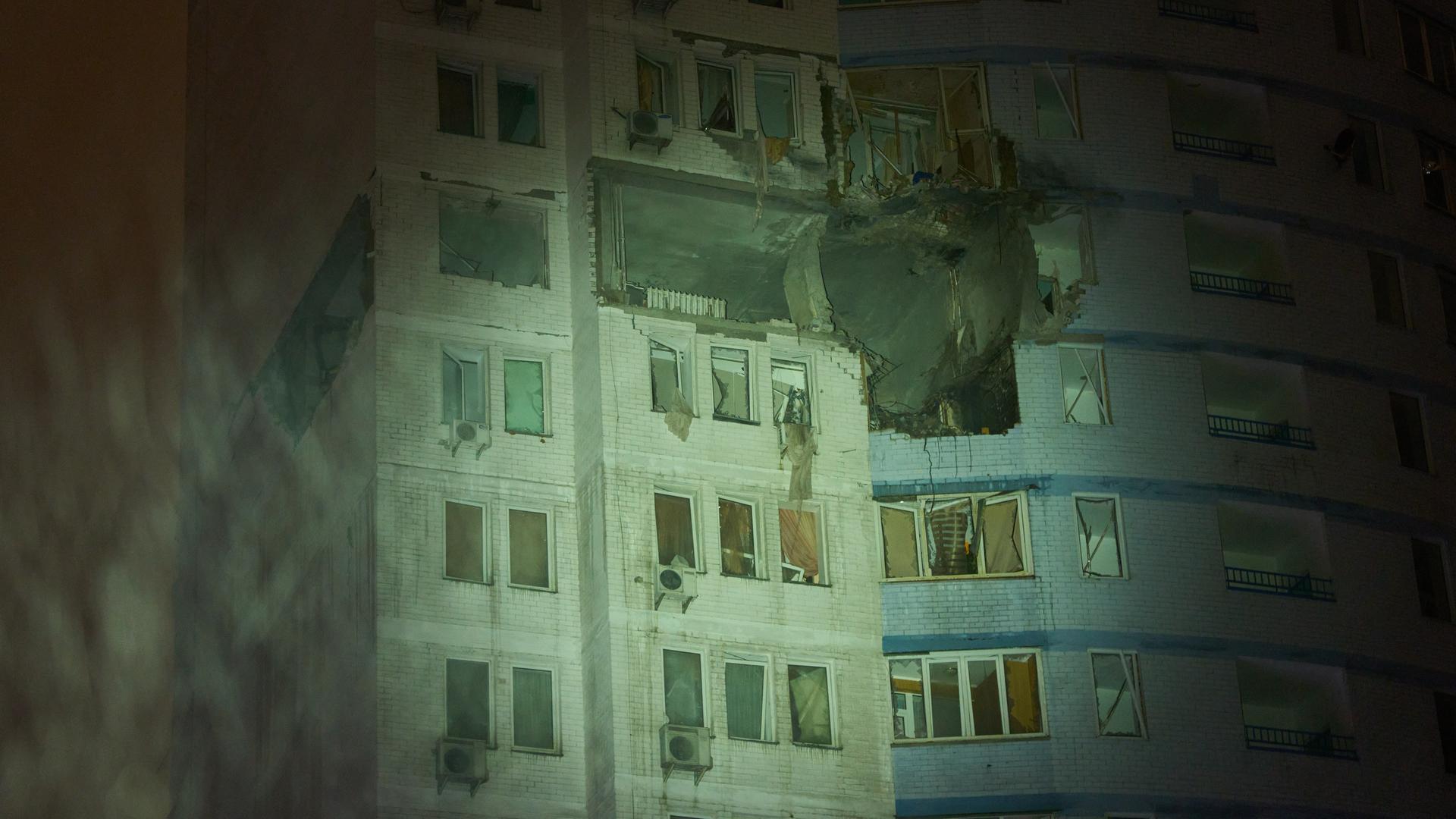 Ein Wohnhaus in Kiew in der Ukraine in der Nacht. Das Haus ist angegriffen worden. Die Fenster sind kaputt. In den Wänden sind Löcher. Es schneit.