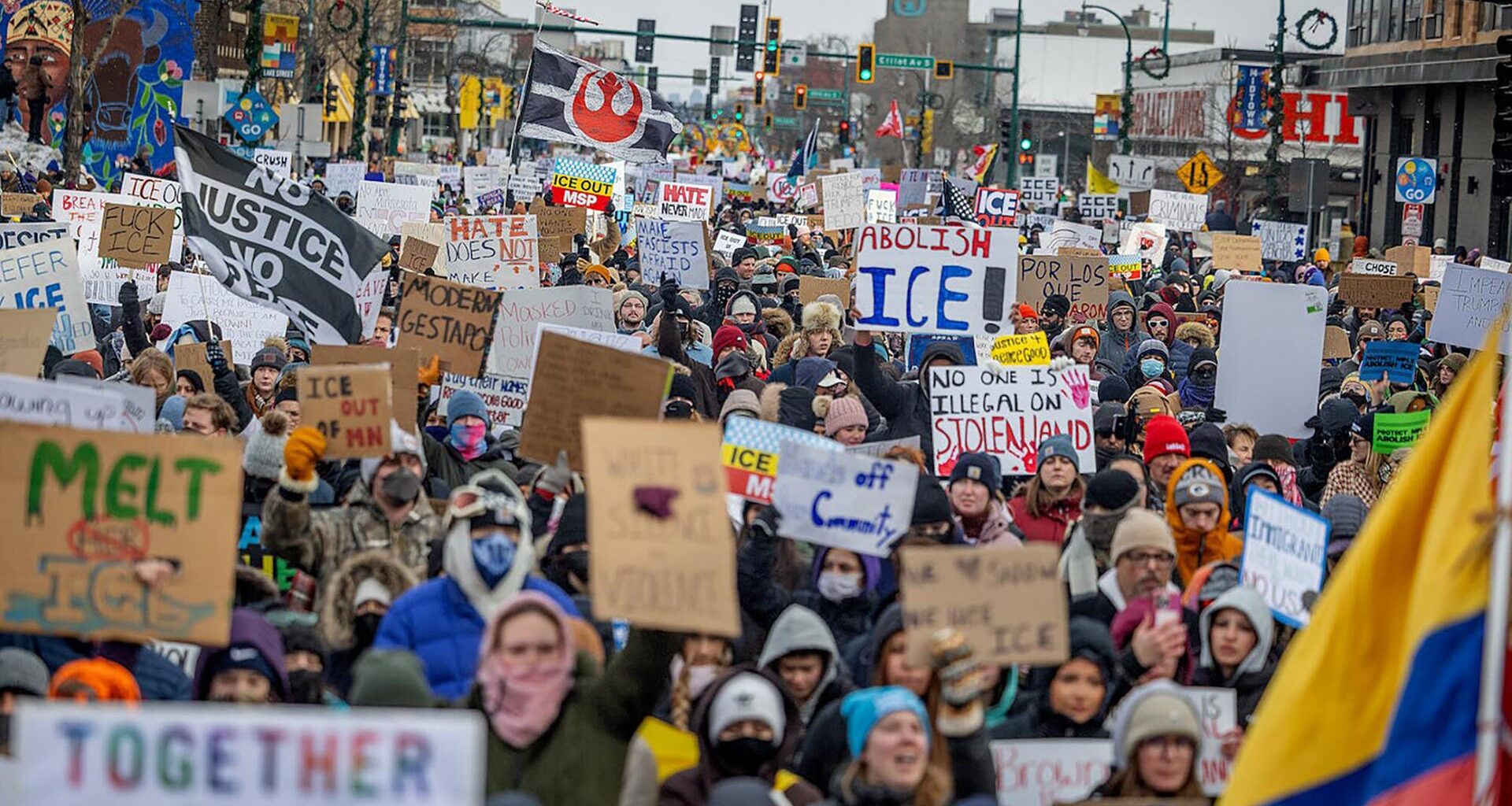 Blick von vorn auf eine riesige Menschenmenge mit Transparenten und Plaketen, die eine Straße entlangläuft.