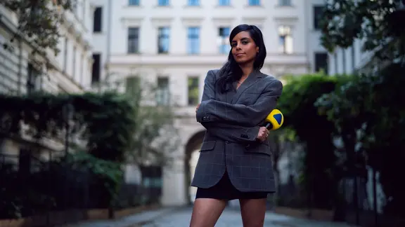 Collien Ulmen-Fernandes mit verschränkten Armen und VIVA-Mikro in der Hand in einem Innenhof | ARD Kultur/Florida Factual, Tom Ballschmieter Collien Ulmen-Fernandes mit verschränkten Armen und VIVA-Mikro in der Hand in einem Innenhof