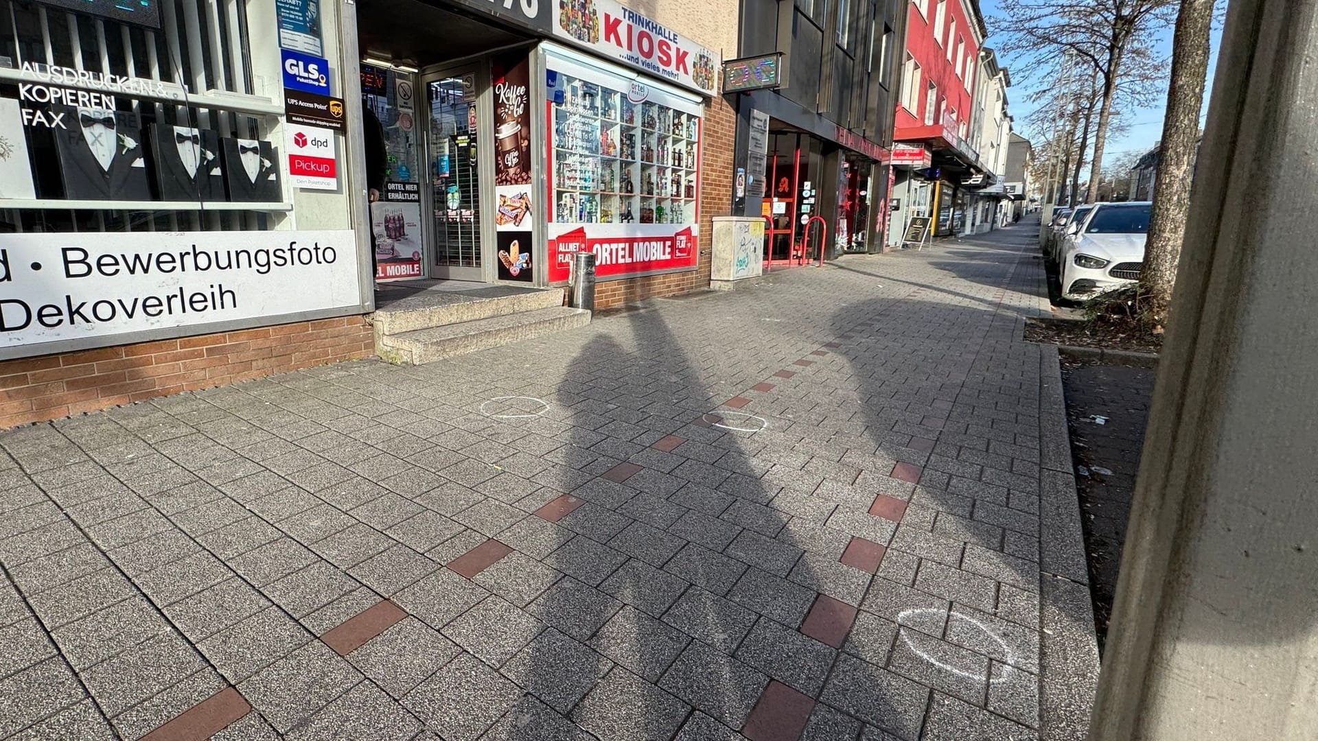 Vor einem Kisok sind Markierungen der Spurensicherung auf dem Bürgersteig. Ein 27-jähriger Mann ist in Dortmund auf offener Straße von mehreren Kugeln getroffen worden.