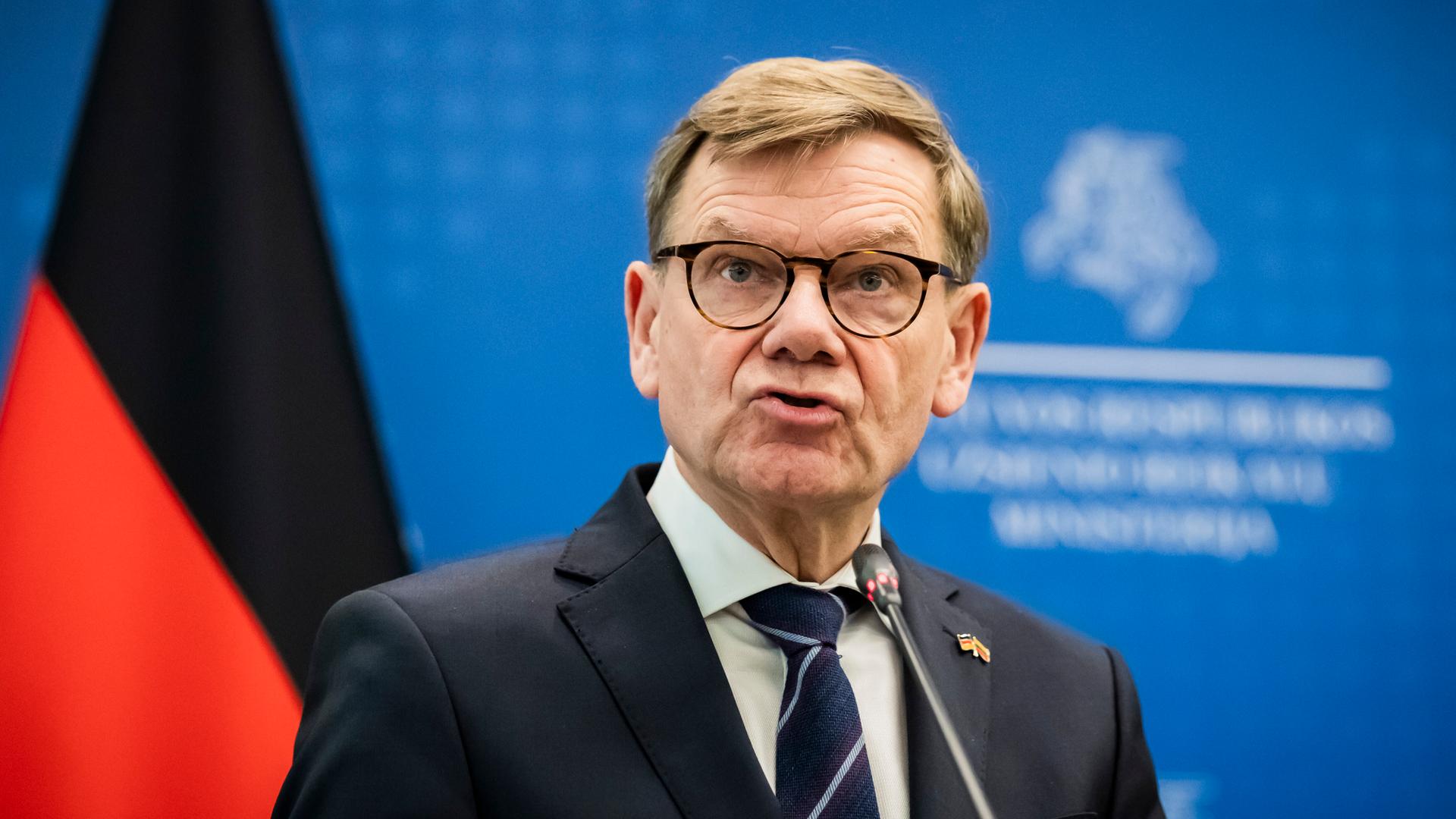 Wadephul steht vor einer blauen Wand mit der deutschen Flagge.