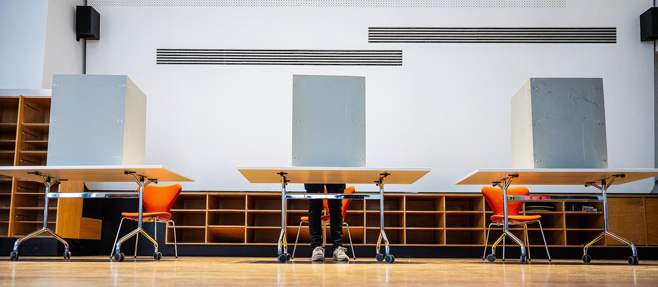 In einem Wahllokal steht ein Mann hinter einer Wahlkabine.