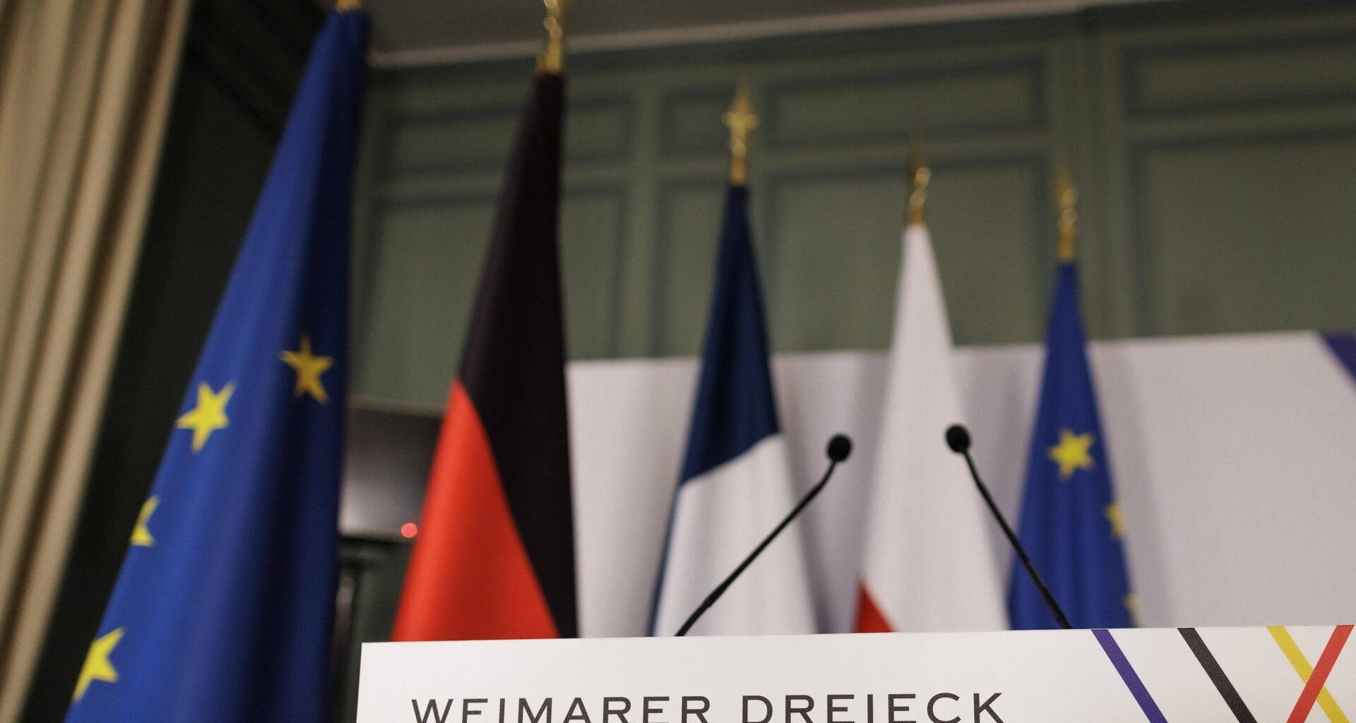 Ein Rednerpult steht vor der Pressekonferenz im Rahmen des Treffen des Weimarer Dreiecks im Schloss de la Celle in La Celle-Saint-Cloud am 12.02.2024 in einem Saal. Dahinter die Länder- und die EU-Fahnen.