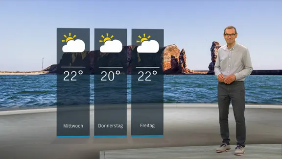 NDR Moderator Meeno Schrader steht im Studio mit der Wettervorhersage.