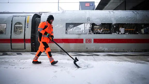 Ein Mann mit einem Schneeschieber auf einem Bahngleis in Hamburg.