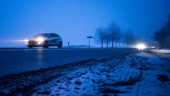  Ein Auto fährt am Morgen über eine teilweise vereiste Bundesstraße.