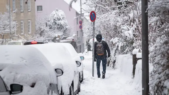 Ein Mann läuft über einen nicht geräumten Gehweg voll Schnee.