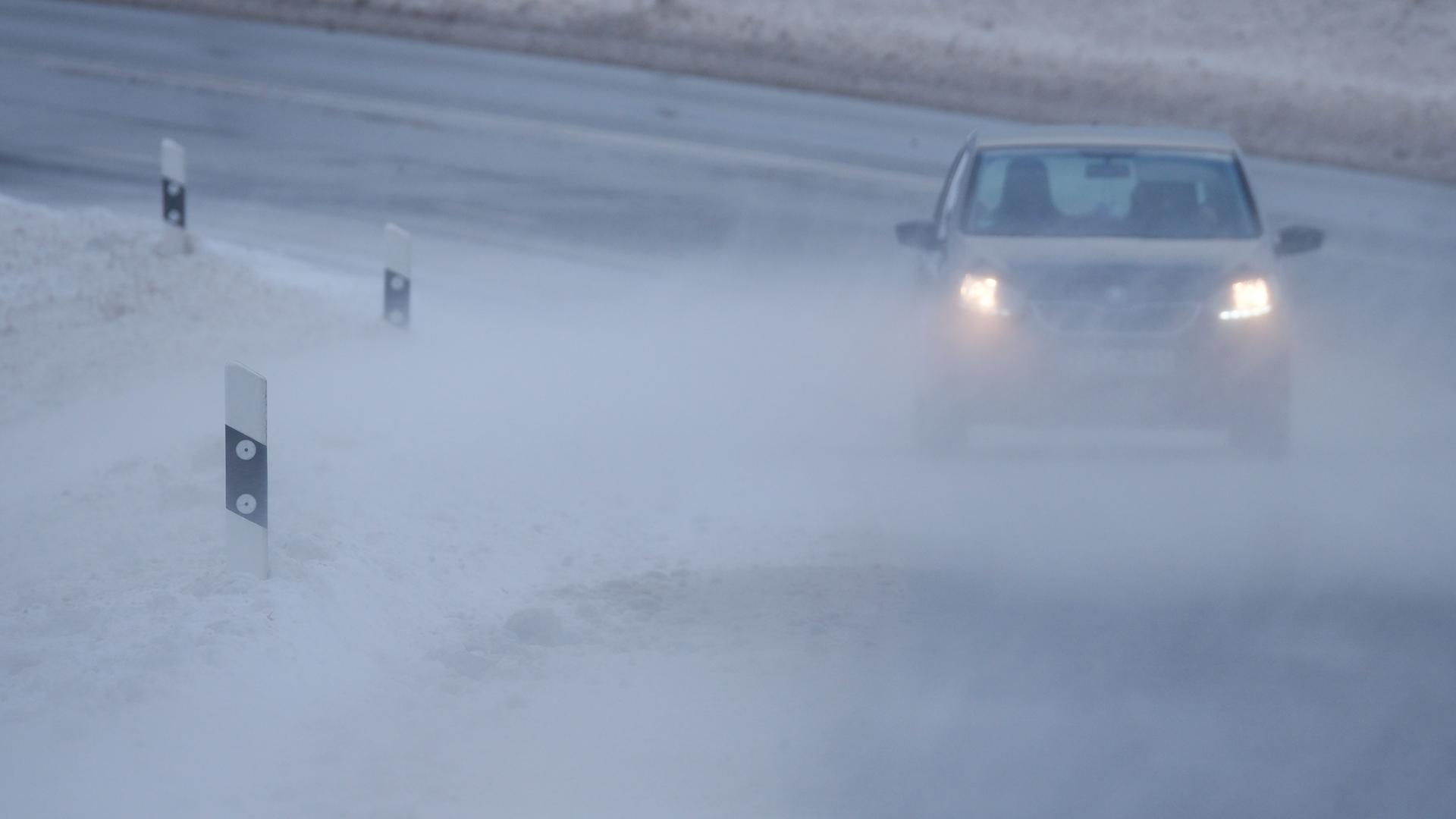Schnee wird über eine Straße geweht, auf der ein Auto fährt. Schnee wird über eine Straße geweht, auf der ein Auto fährt.