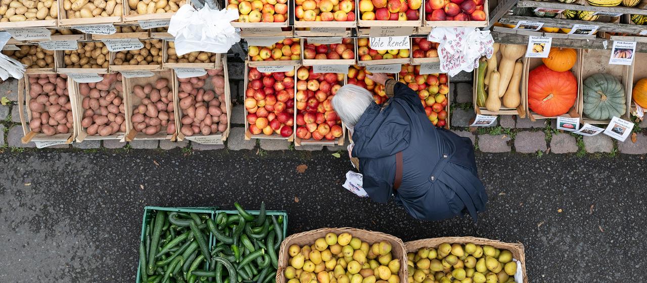 Eine Frau steht auf einem Wochenmarkt an einem Stand mit Obst und Gemüse. | dpa Eine Frau steht auf einem Wochenmarkt an einem Stand mit Obst und Gemüse.