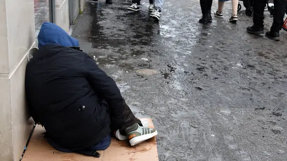 Ein Mensch sitzt im Winter auf einer Straße auf einem Pappkarton