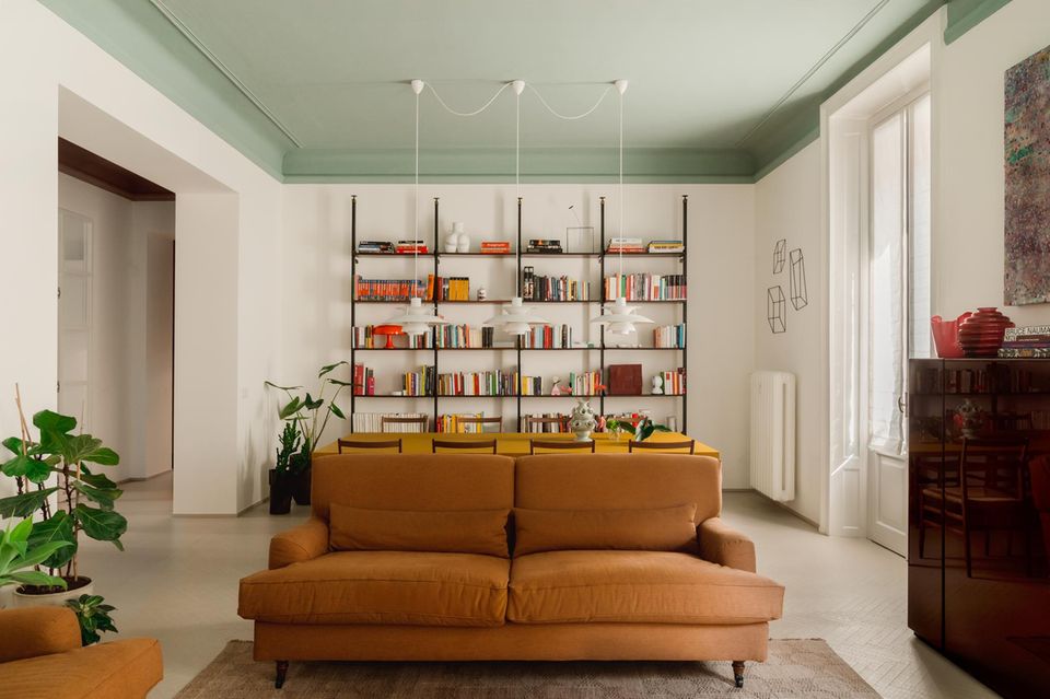 Cognacfarbenes Sofa, dahinter ein Esstisch und großes Bücherregal