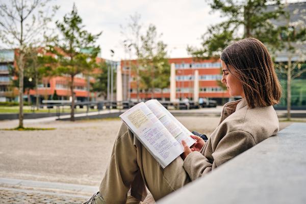 Studierende beim Lernen mit Buch auf dem Campus